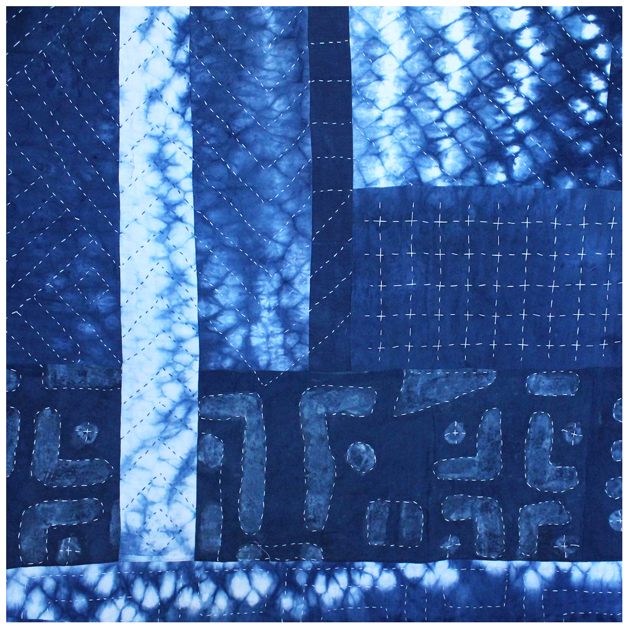 A detail view of a handmade indigo dyed patchwork quilt, showing off delicate hand stitching patterns.