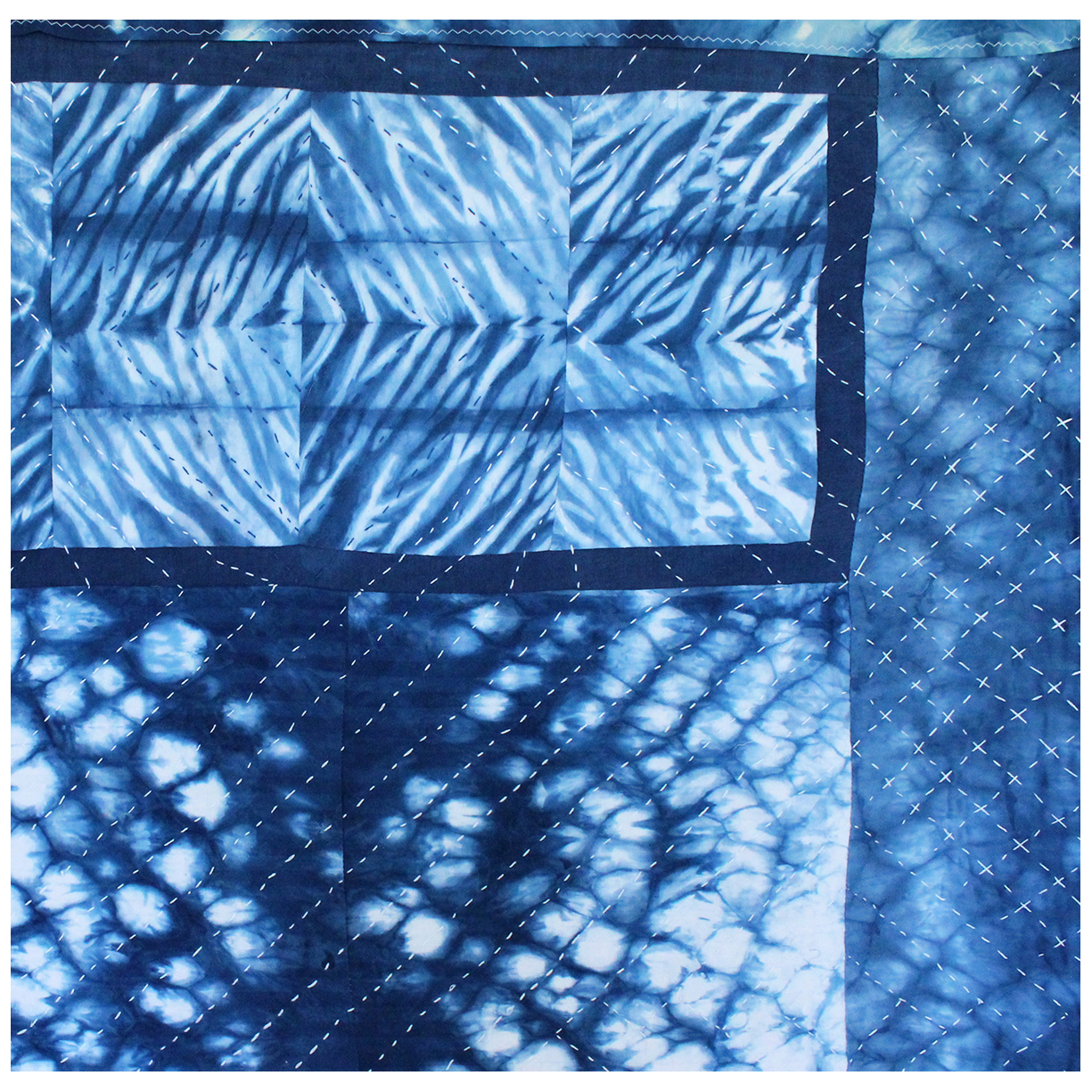 A detail view of a handmade indigo dyed patchwork quilt, showing off delicate hand stitching patterns.