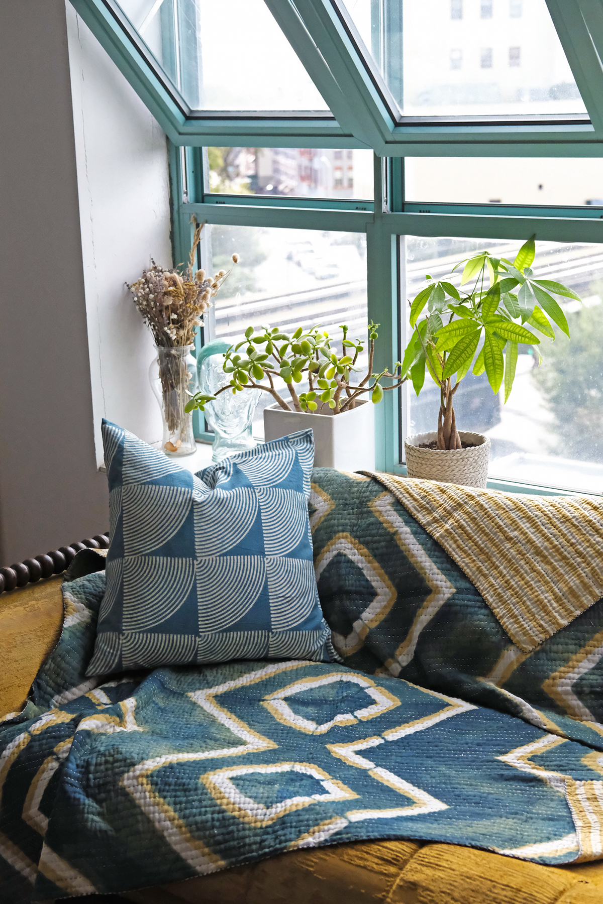 Mirage quilt with Wifi Pillow on a couch next to a big window with plants