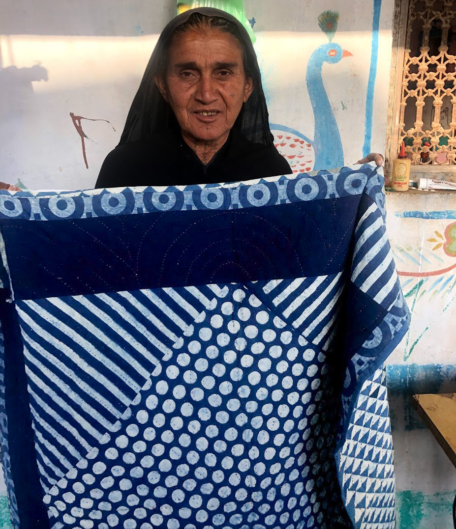 Indian artisan holding up the indigo quilt she worked on